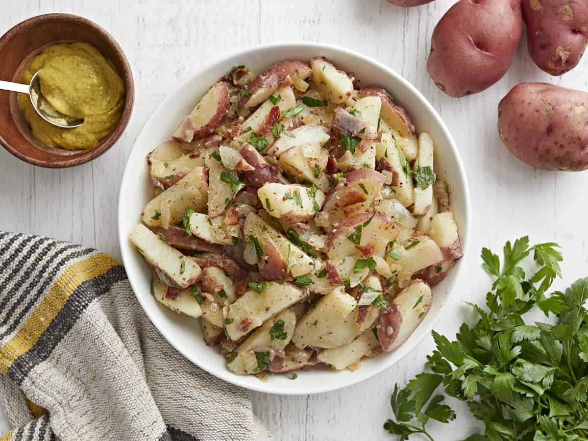 German Potato Salad is tossed in a deliciously sweet and tangy mayo-free dressing with bacon, mustard, and vinegar. Perfect for potlucks! BudgetBytes.com Overhead view of German Potato Salad in a bowl.