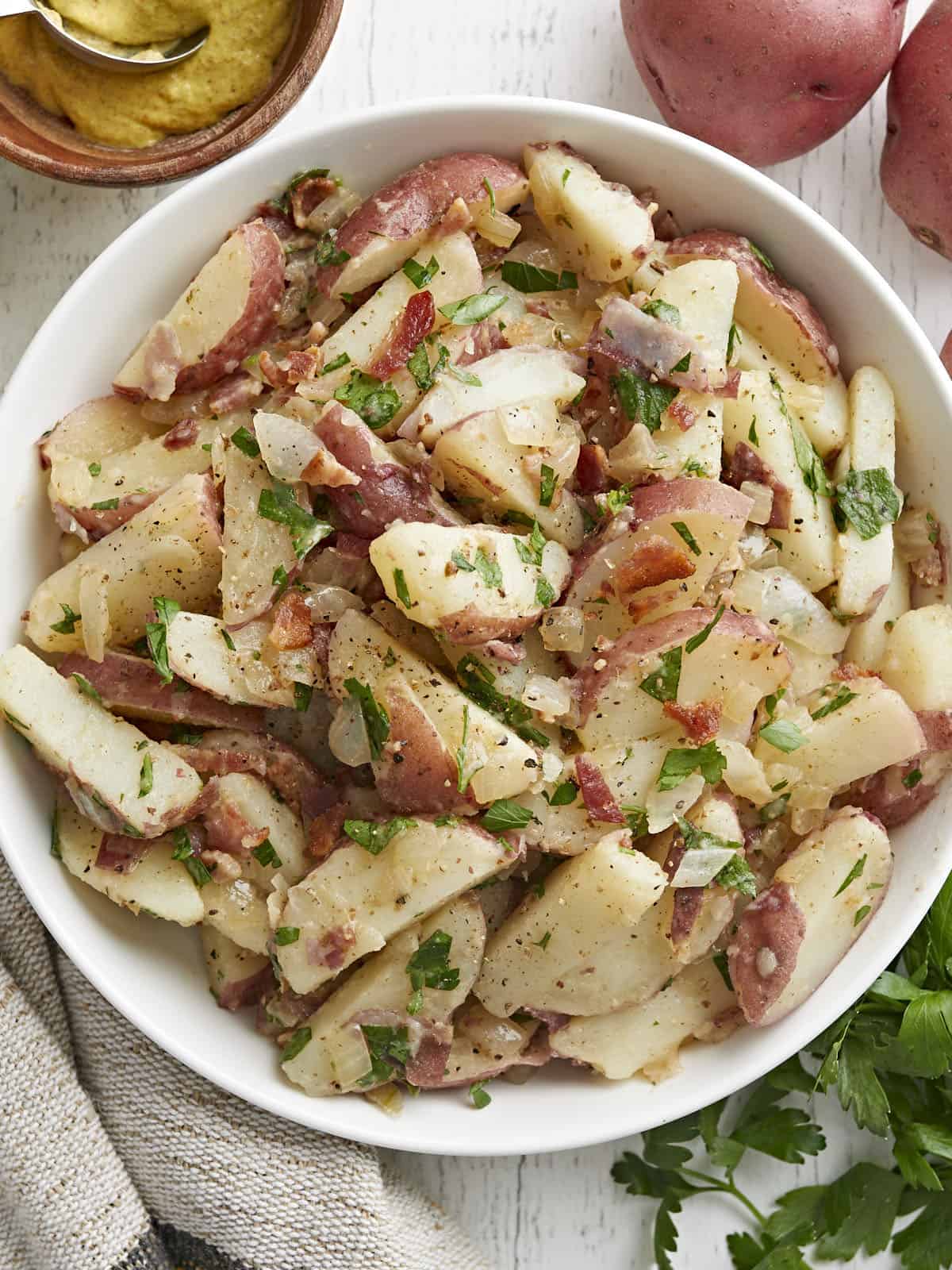 German Potato Salad is tossed in a deliciously sweet and tangy mayo-free dressing with bacon, mustard, and vinegar. Perfect for potlucks! BudgetBytes.com close up overhead view of German potato salad in a bowl.