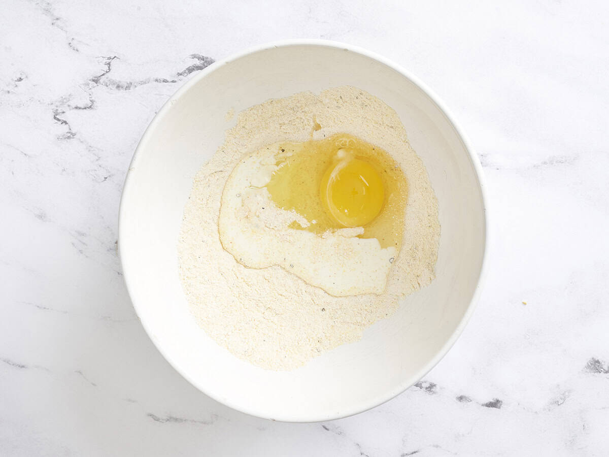 An egg and heavy cream added to a mixing bowl with dry ingredients for sweet corn fritters.