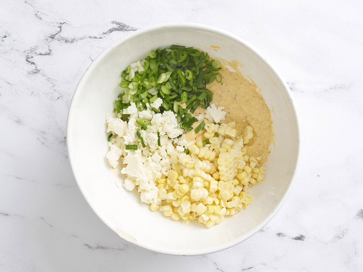 Sliced green onions, crumbled feta cheese and fritter batter in a bowl.