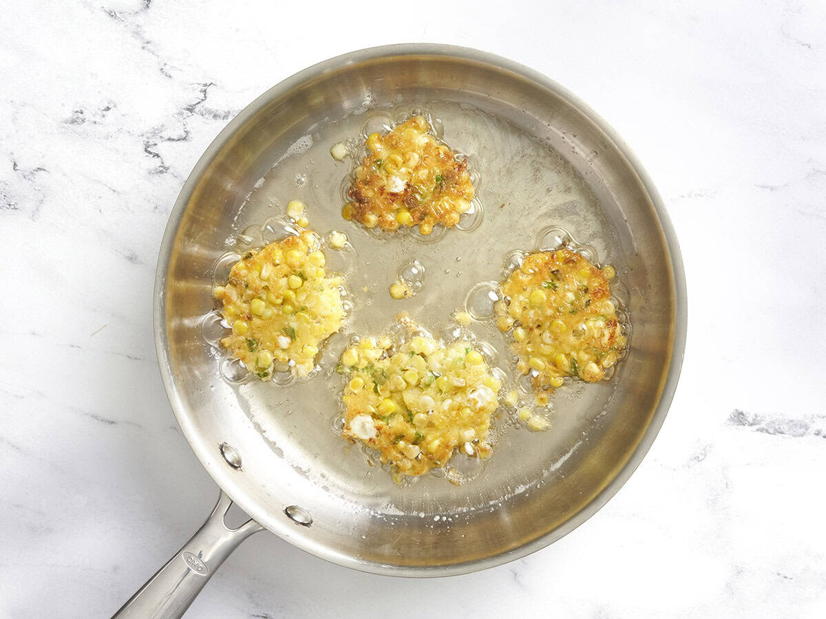 Flipped sweet corn fritters in a skillet with oil.