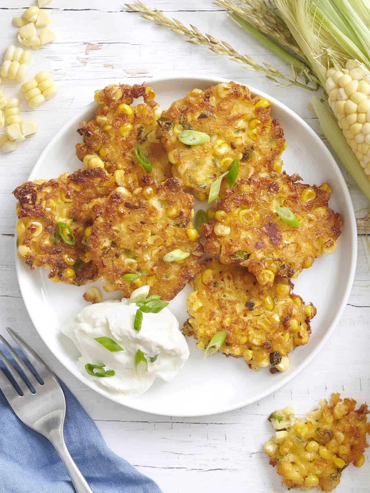 Overhead view of sweet corn fritters on a plate with sour cream and green onions.
