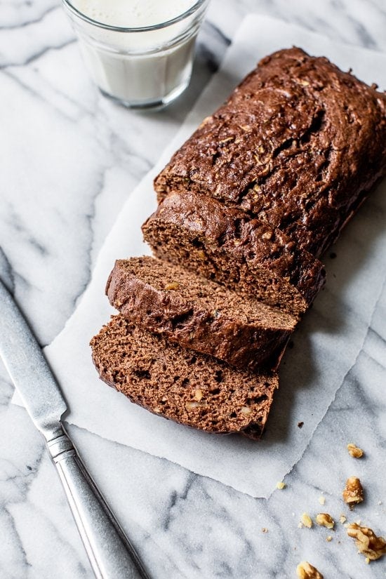 This Chocolate Zucchini Bread is so rich and delicious, no one will guess that it's secretly healthy! Add walnuts for crunch in every bite. Sliced Chocolate Zucchini Bread loaf on white marble