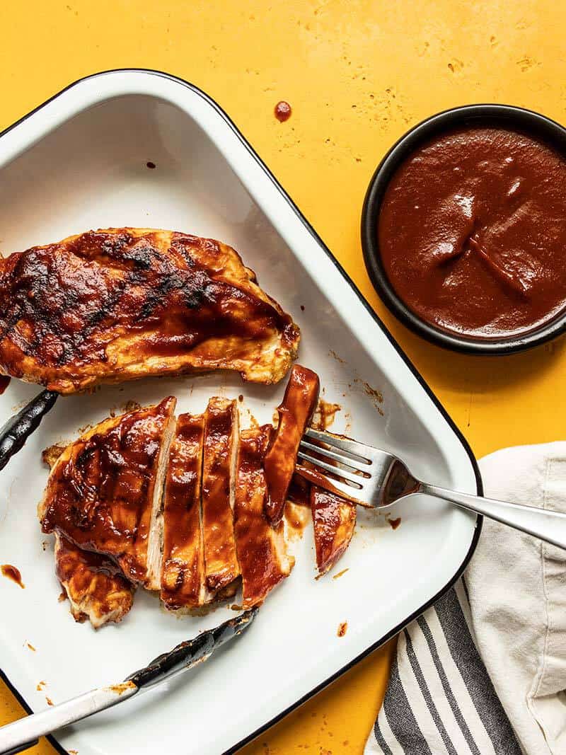 This sweet, tangy, and rich homemade bbq sauce takes only minutes to make, uses no bottled ketchup, and is great for more than just grilling! Budgetbytes.com BBQ chicken breasts in a white dish, one sliced into strips, and a bowl of homemade bbq sauce on the side.