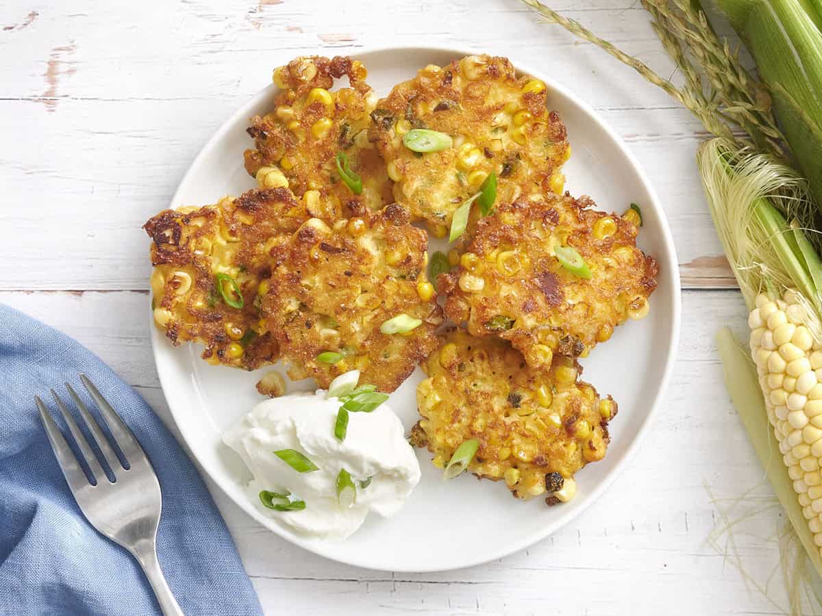 Overhead view of sweet corn fritters on a plate with sour cream and green onions.