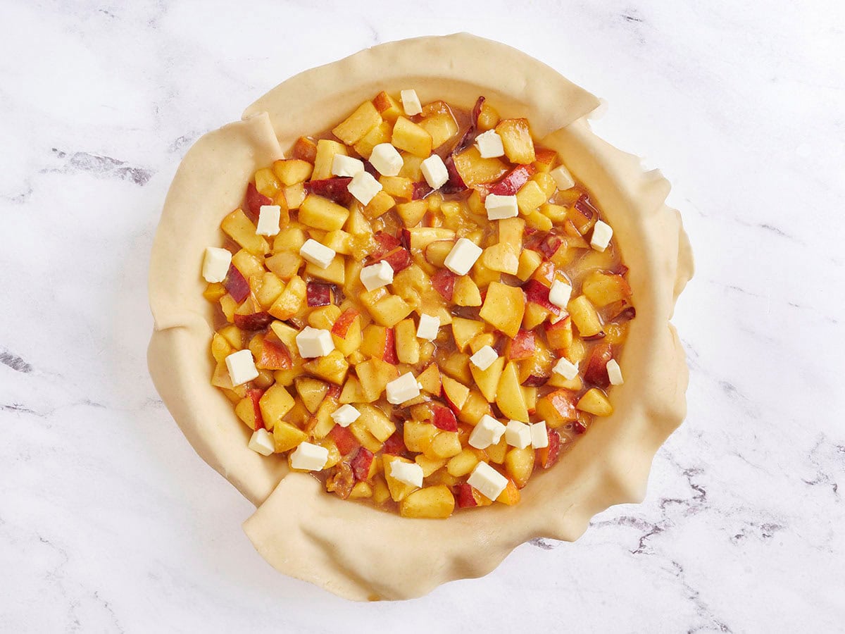 Peach pie filling in a pie dish topped with butter.