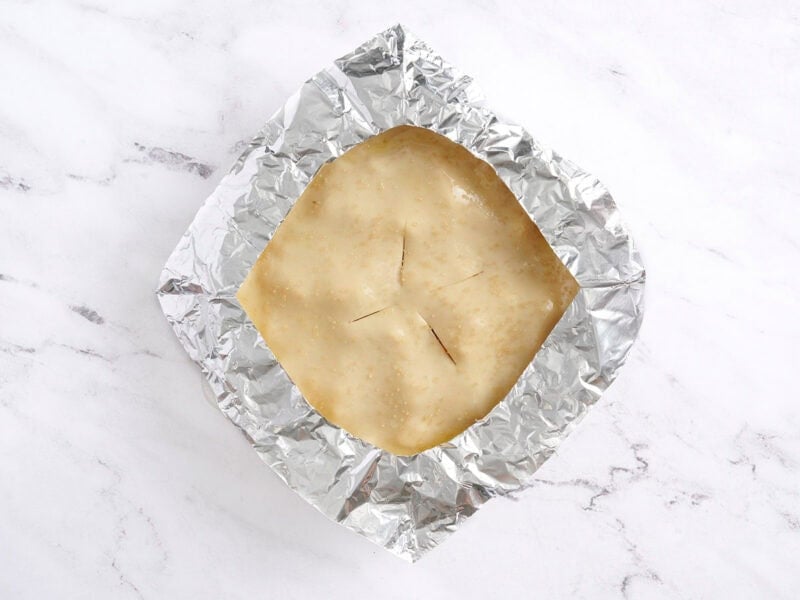 An unbaked homemade peach pie topped with a foil collar.