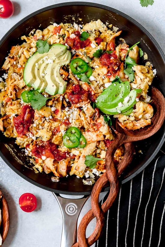 Migas are a classic Tex Mex breakfast recipe, but you can enjoy them anytime of day! Eggs, tortillas, cheese and veggies make them satisfying. Overhead view of Tex Mex migas in skillet with sliced avocado