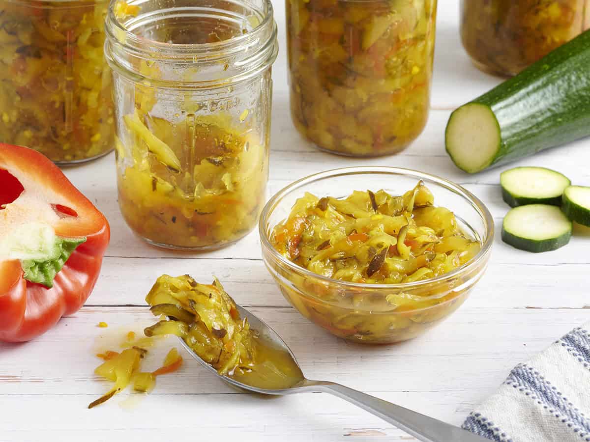 Jars of homemade zucchini relish, with some in a small bowl next to the first jar.