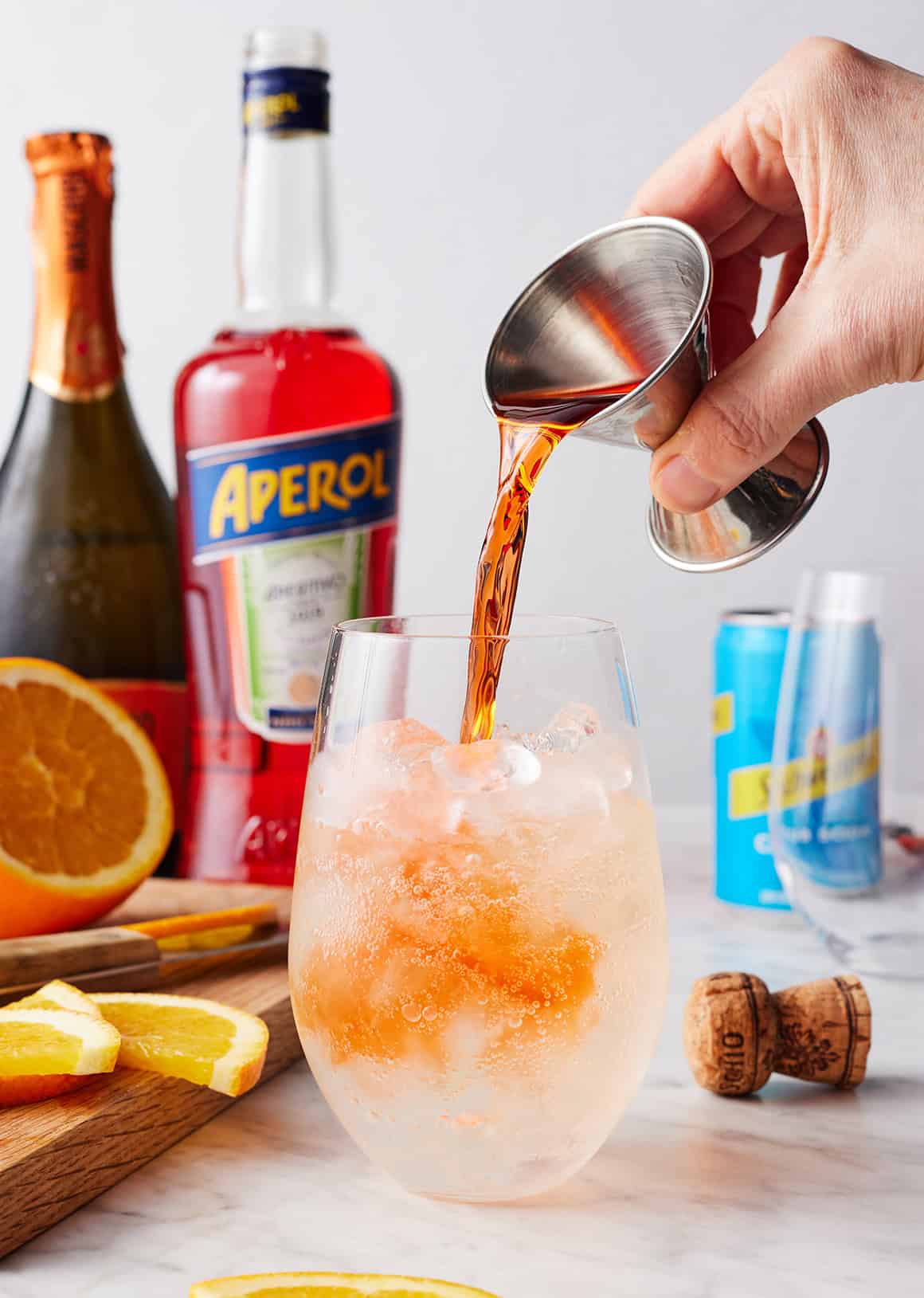 Pouring aperol into wine glass filled with prosecco and ice