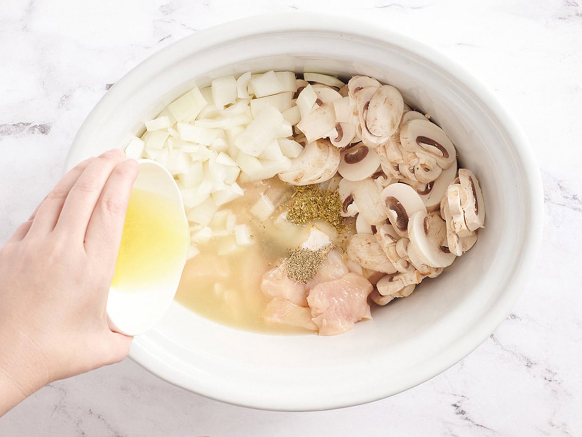 Cubed chicken, onions, mushrooms, seasonings, and chicken broth in a crockpot.