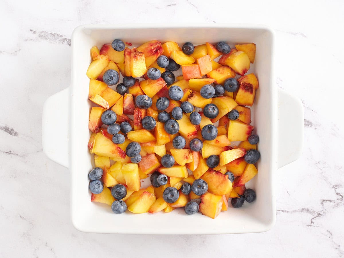 Diced peaches and blueberries in a baking dish.
