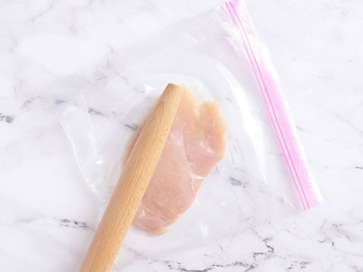 A chicken breast cutlet being pounded with a rolling pin.