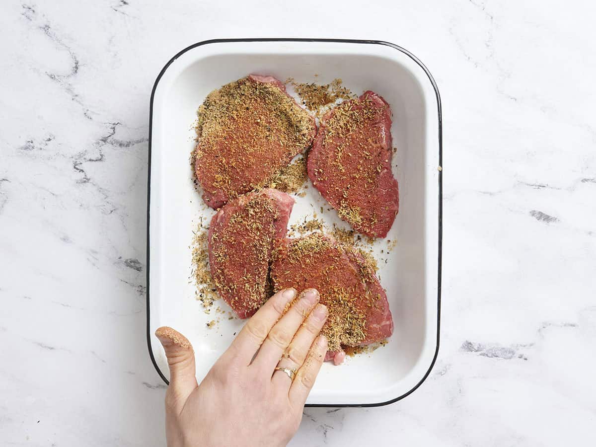 A hand seasoning four sirloin tenders in a baking dish.
