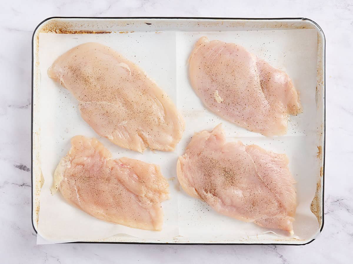 Four chicken breast cutlets on a parchment lined baking sheet.