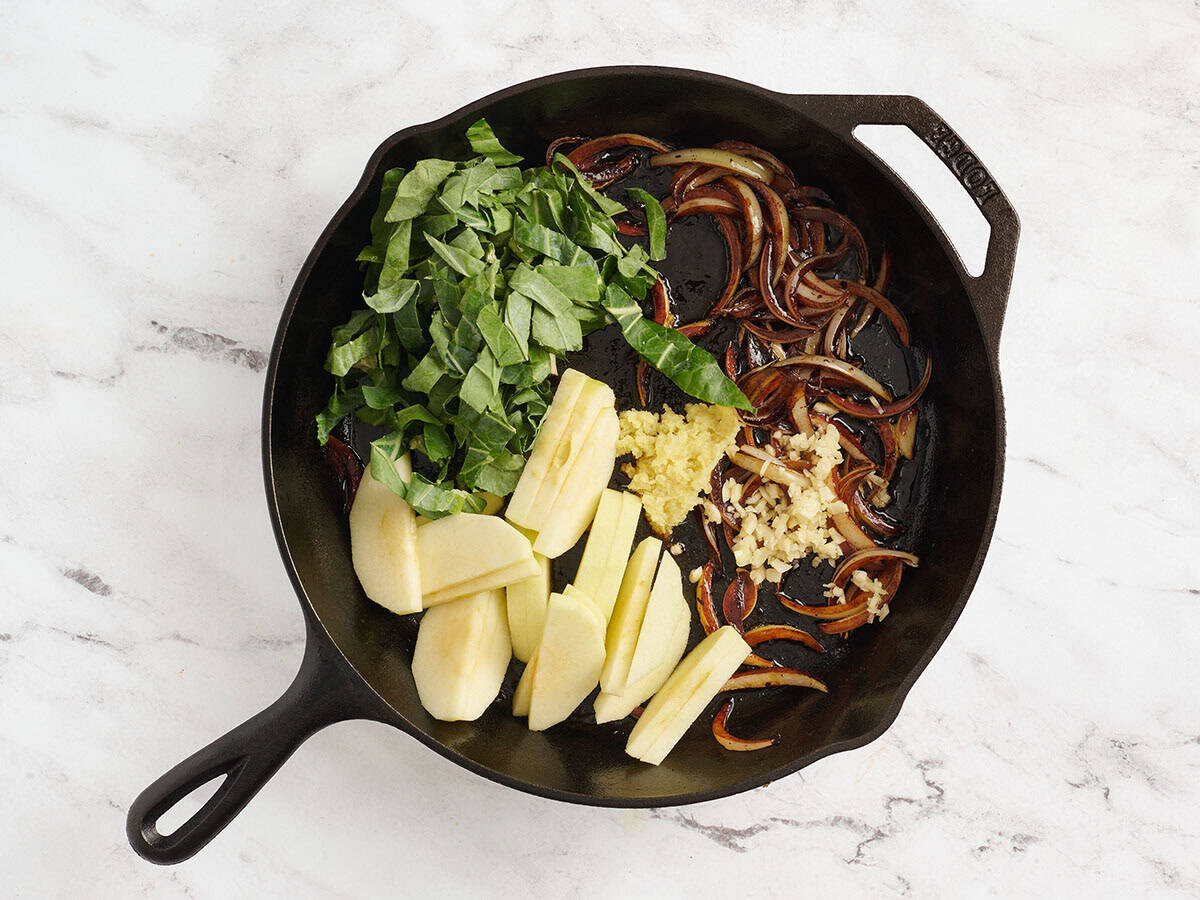 Collard greens, sliced apple, grated ginger, and minced garlic added to a skillet with sauteed onions.