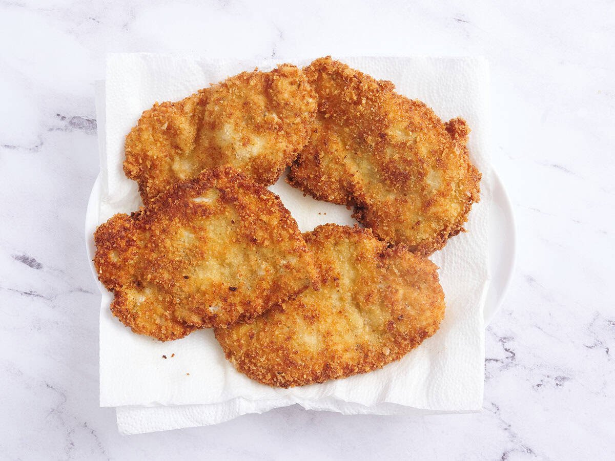 Four chicken schnitzels resting on paper towels.