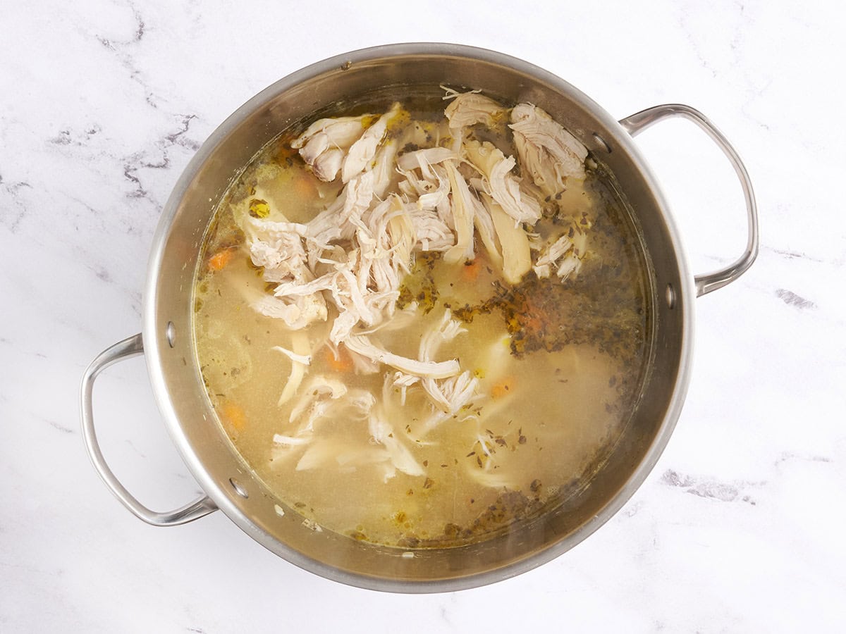 Shredded chicken added to a pot of chicken noodle soup.