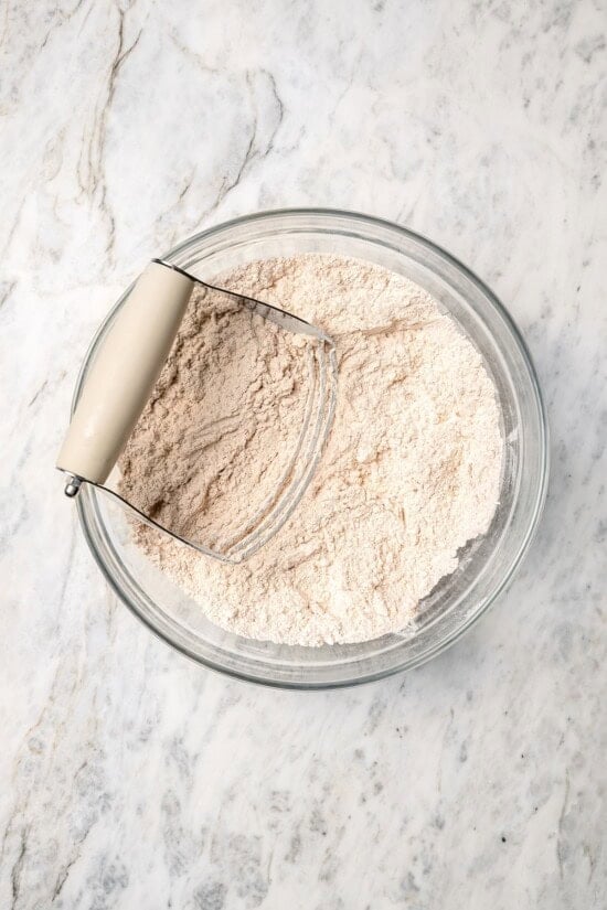 Overhead view of dry ingredients for apple scones in glass bowl with pastry cutter