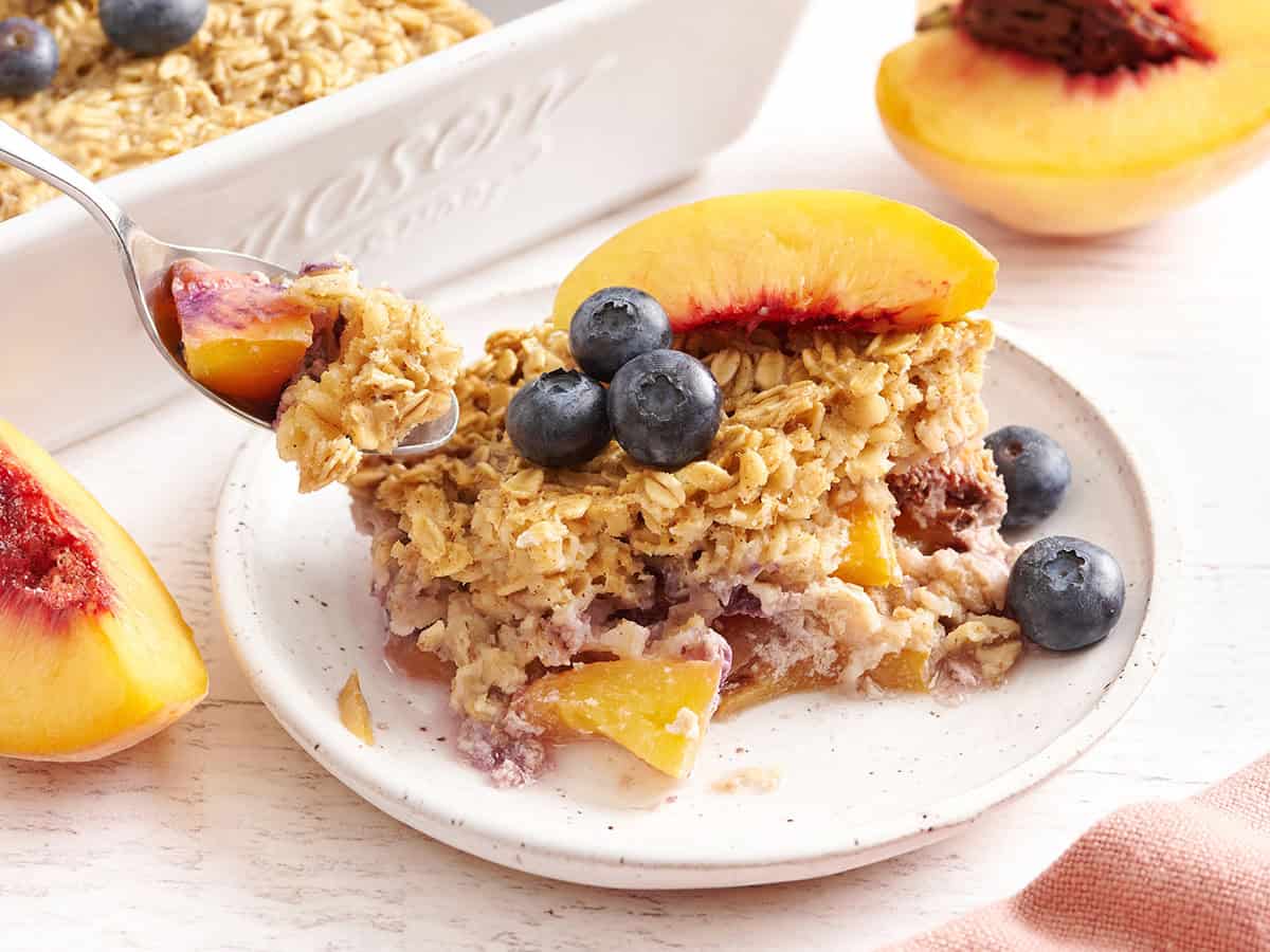 Side view of peach and blueberry baked oatmeal on a plate with a spoon taking some.
