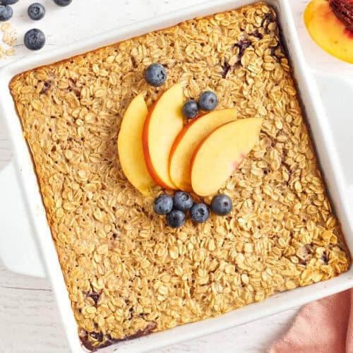 Overhead view of a baking dish of baked oatmeal topped with peach slices and blueberries.