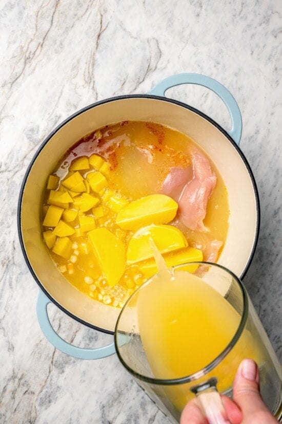 This rich, creamy Chicken Corn Chowder is thickened with potatoes and pureed corn instead of heavy cream to keep it light. Easy and delicious! Pouring broth into dutch oven for chicken corn chowder.