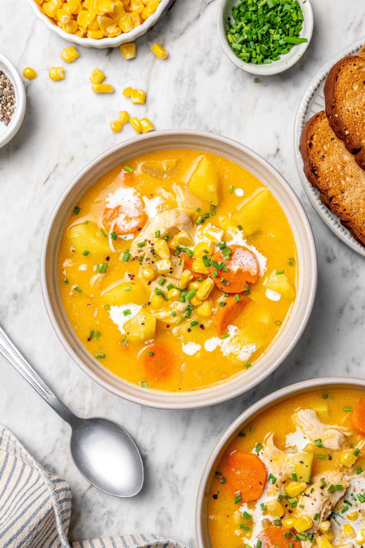 This rich, creamy Chicken Corn Chowder is thickened with potatoes and pureed corn instead of heavy cream to keep it light. Easy and delicious! Two bowls of creamy chicken corn chowder on marble tabletop.