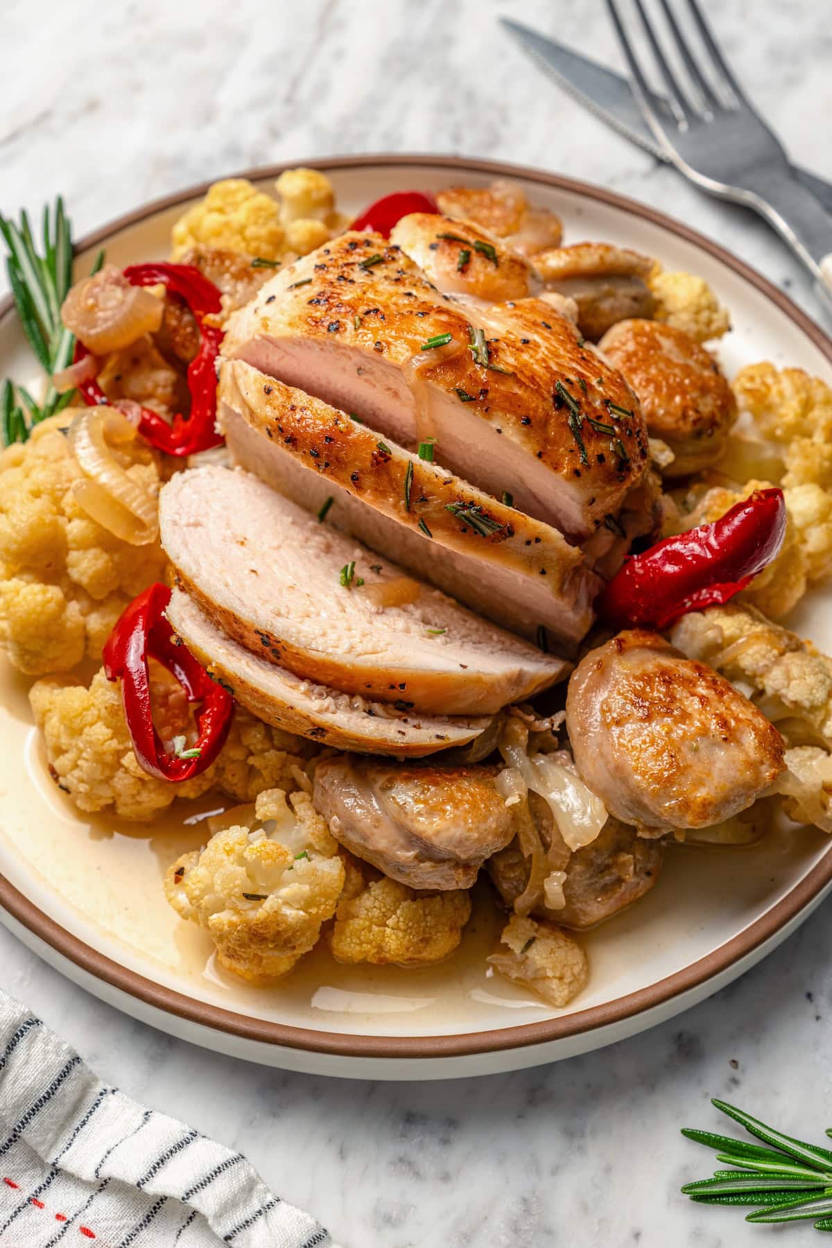 Sliced chicken scarpariello on plate with sausage and cauliflower.
