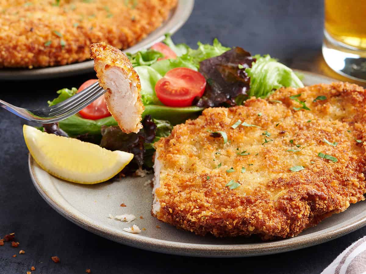 Side view of a chicken schnitzel on a plate with a fork taking a slice.