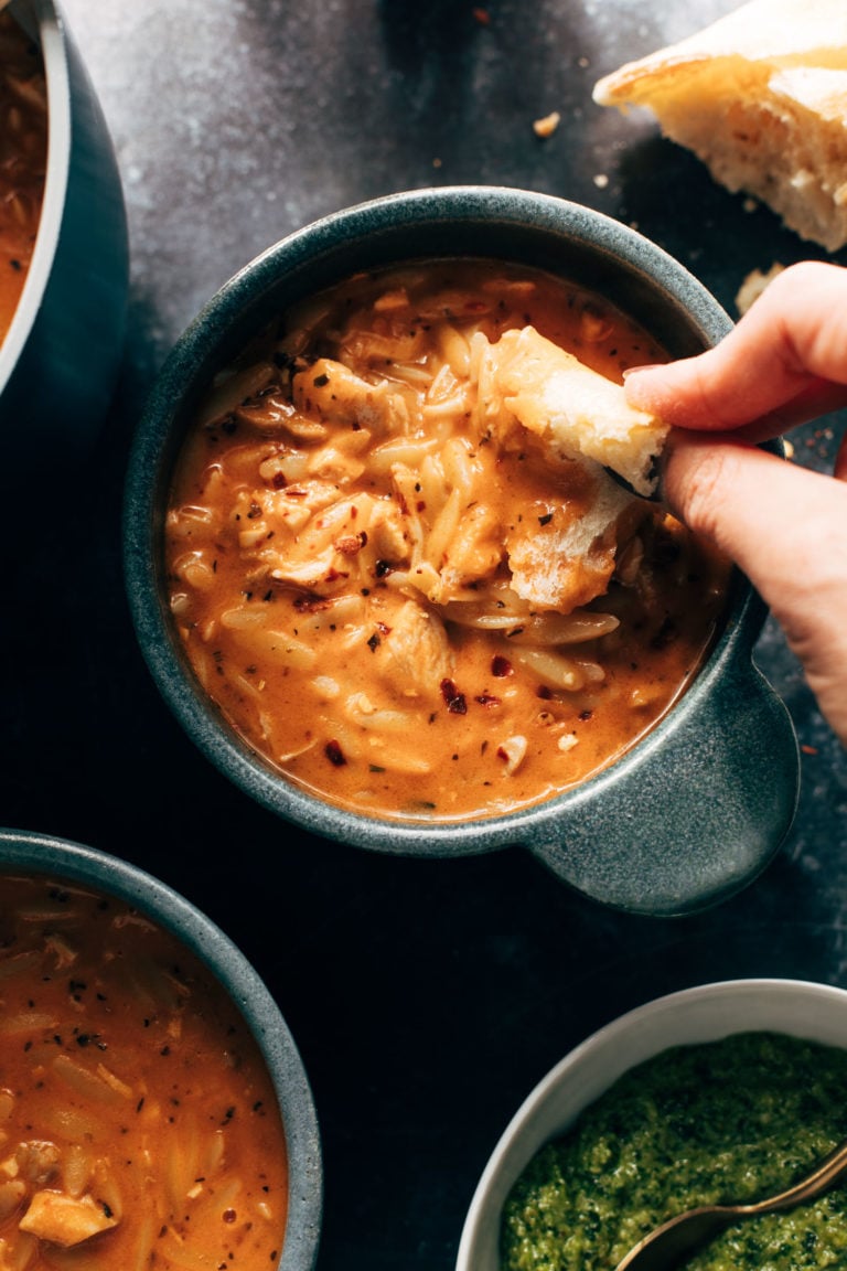 Chicken and orzo tomato soup in a bowl with bread being dipped in.