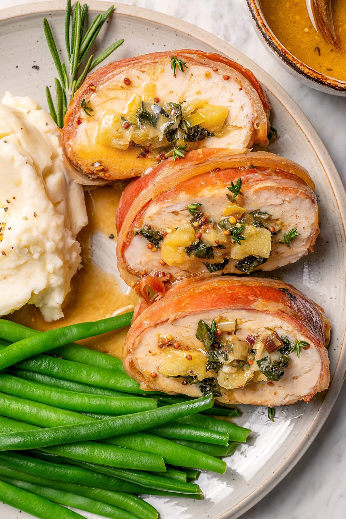 This Prosciutto Wrapped Stuffed Turkey Tenderloin recipe is filled with apples, cheese and kale for a healthy high-protein dinner. Delicious! Plate with prosciutto-wrapped stuffed turkey tenderloin, green beans, and mashed potatoes.