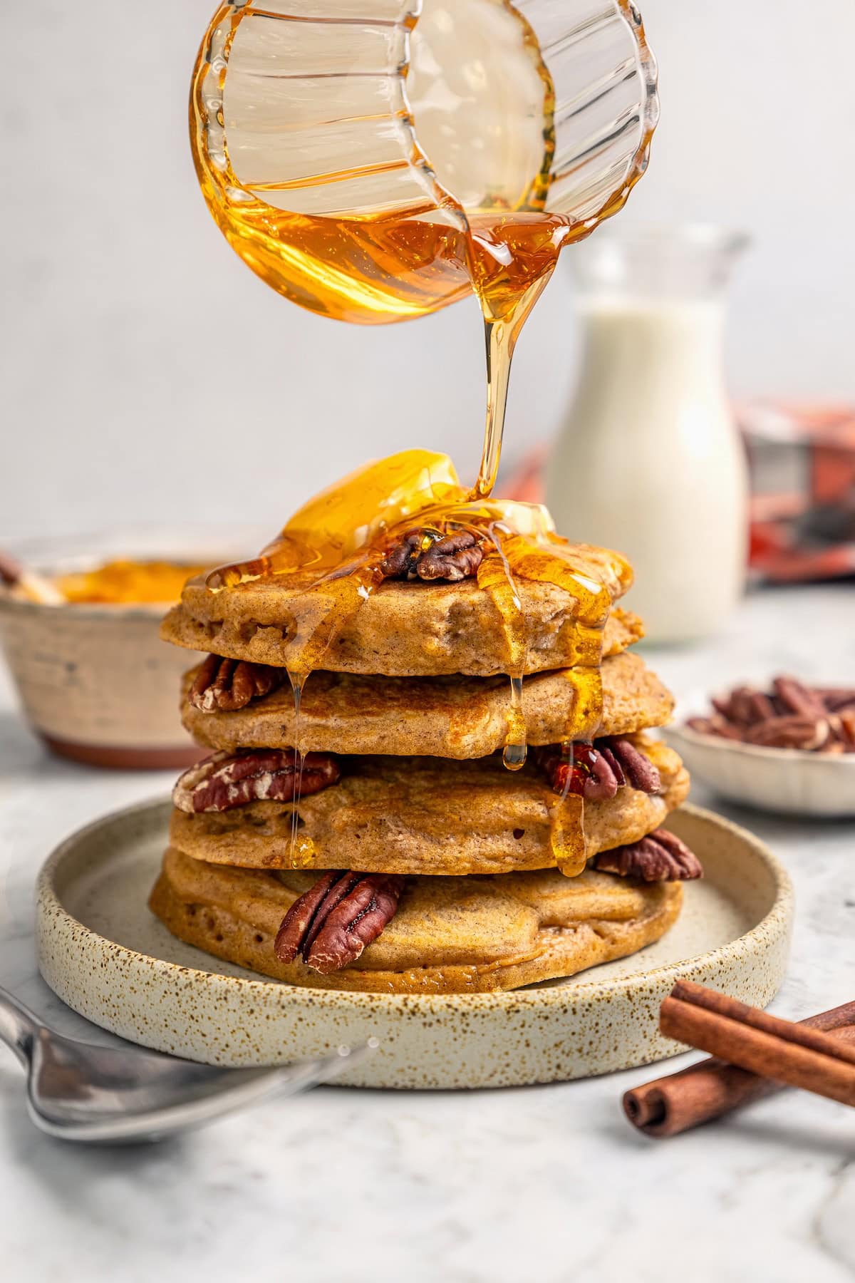 This lightened up version of pumpkin pancakes is also extra fluffy! You'll love the cozy fall flavor in this easy, healthier pancake recipe. Pouring syrup over stack of pumpkin pancakes on plate