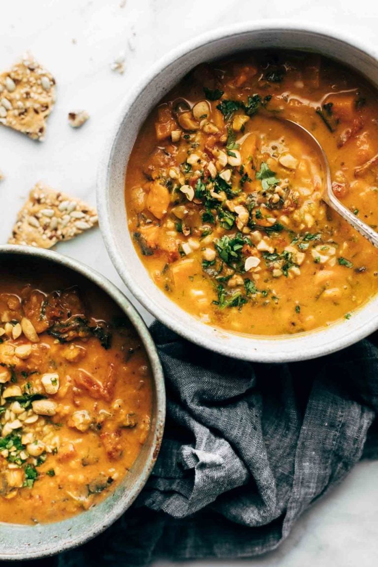 Peanut soup in a bowl with herbs and peanuts on top.