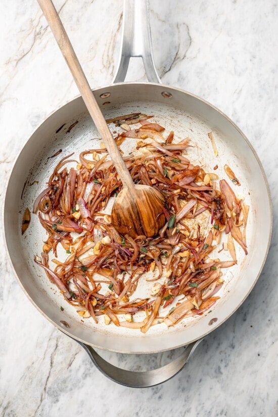 Shallots cooking in skillet with wooden spoon.
