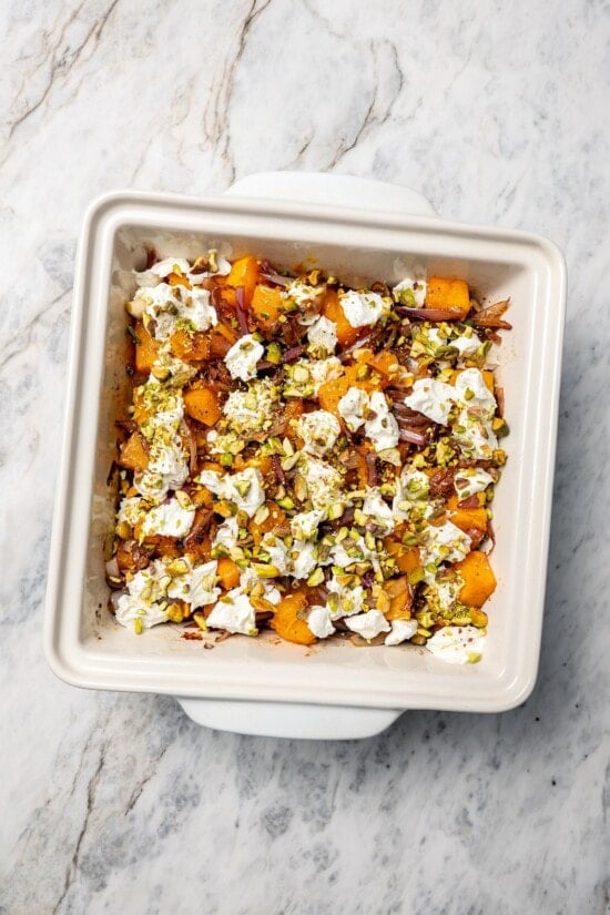 Baked butternut squash in baking dish with goat cheese, pistachios, and shallots.