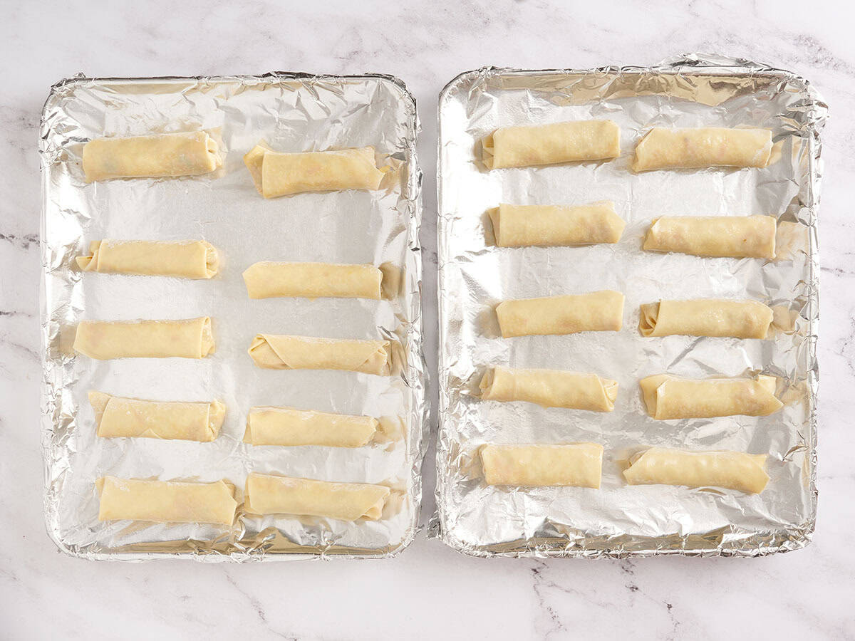 Homemade egg rolls on a foil lined baking sheet before baking.