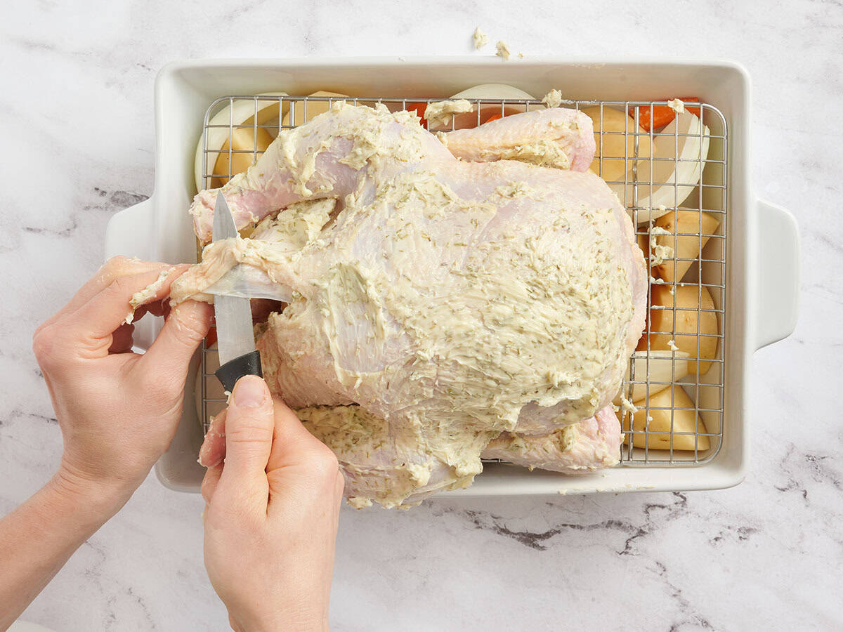 A knife piercing the skin on a whole chicken.