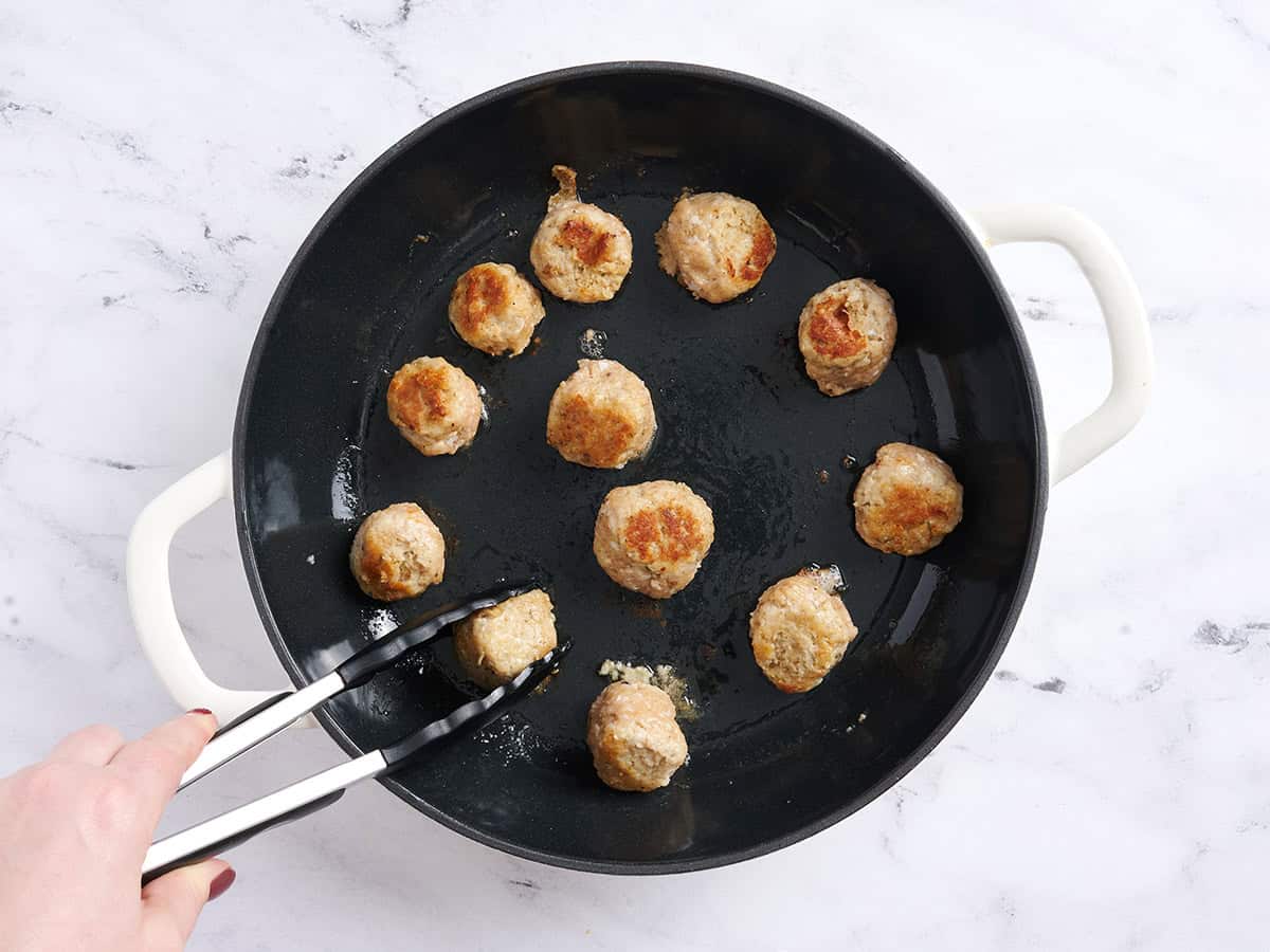 Chicken meatballs cooking in a skillet.