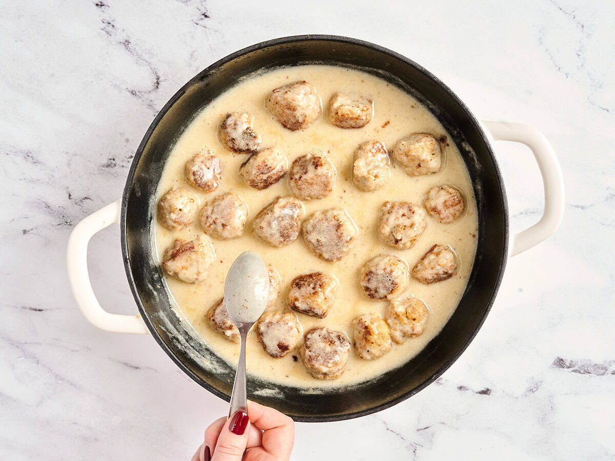 Chicken meatballs in cream sauce in a skillet, with a spoon showing the thickness of the sauce.