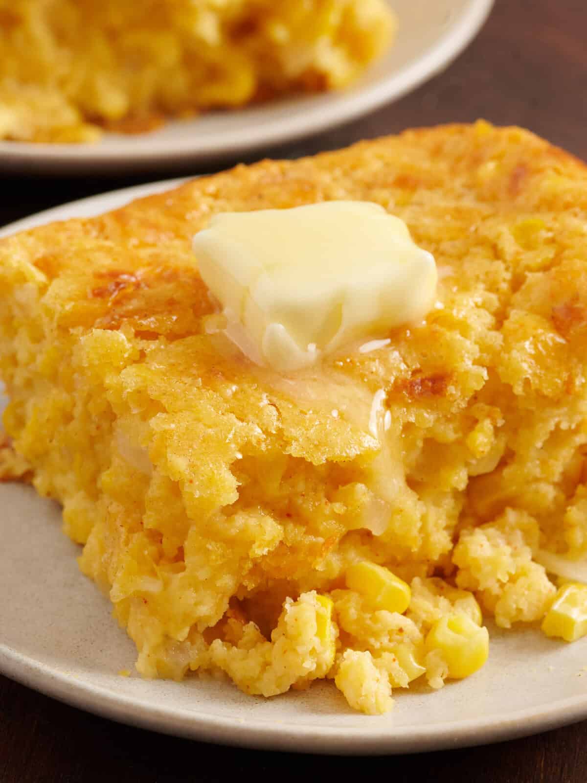 Cornbread casserole on a white plate with a pat of melting butter.