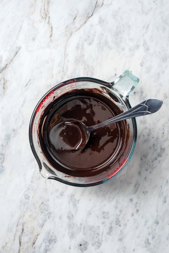 Melted chocolate in liquid measuring cup with spoon.