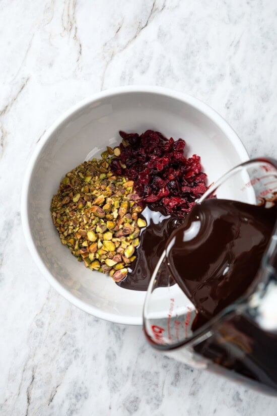 Pouring melted chocolate into bowl with pistachios and cranberries.