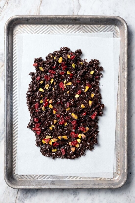 Dark chocolate bark with pistachios and cranberries on parchment paper.