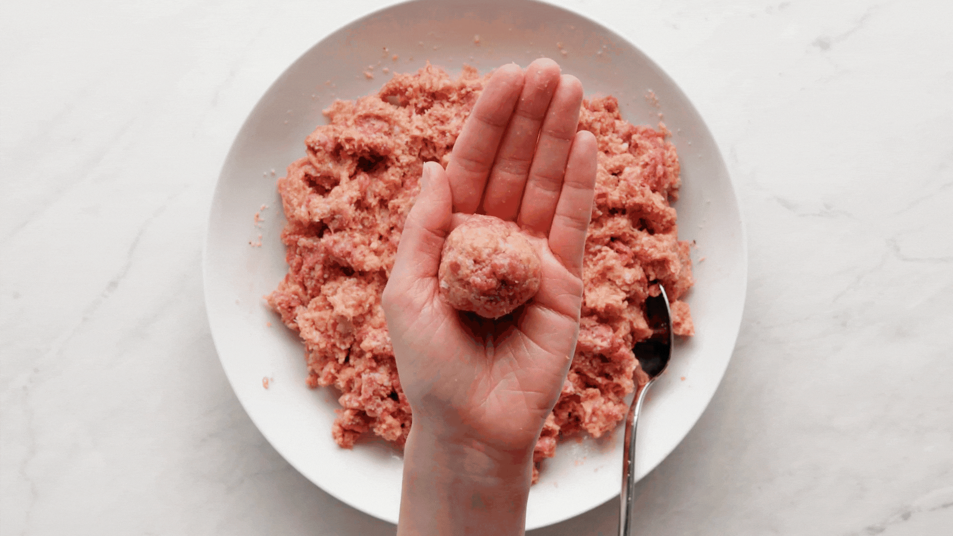 Ground beef and italian seasoning mixture formed into meatballs on a parchment lined baking sheet.
