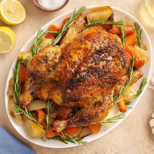 A whole oven roasted chicken on a platter with vegetables.