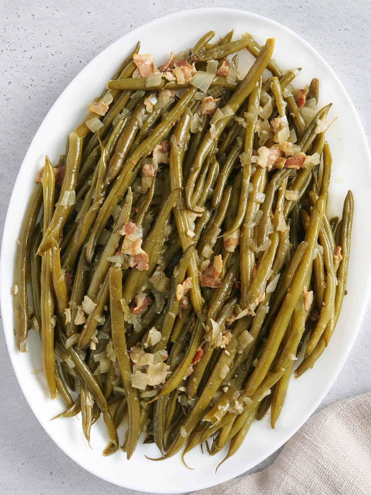 White platter with green beans, onions, and bacon.