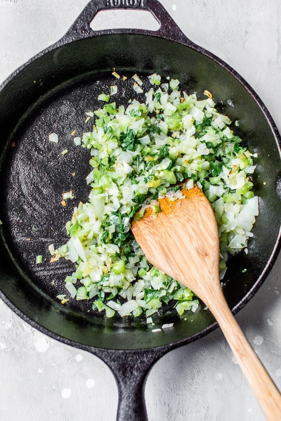 Onions cooking with herbs in a black skillet.