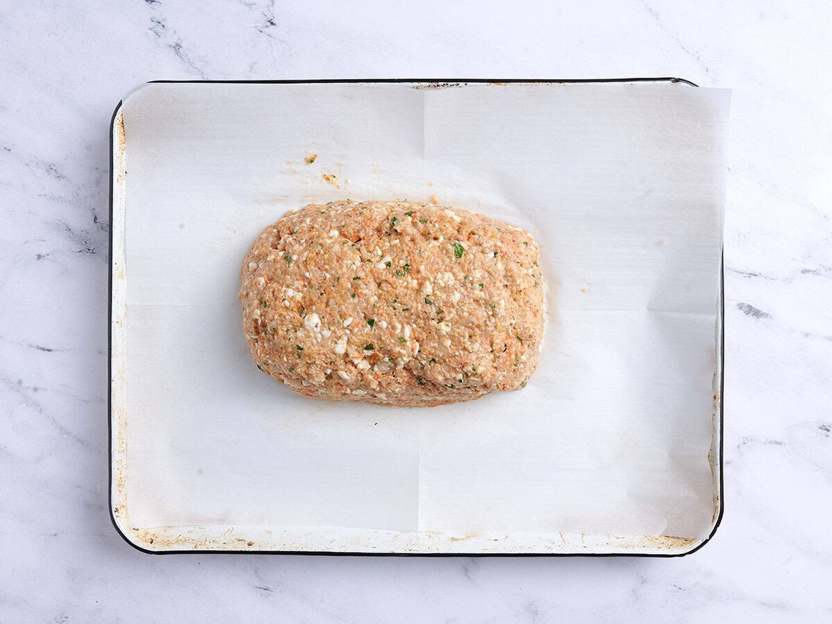Chicken meatloaf shaped into a loaf on a baking sheet lined with parchment paper. 