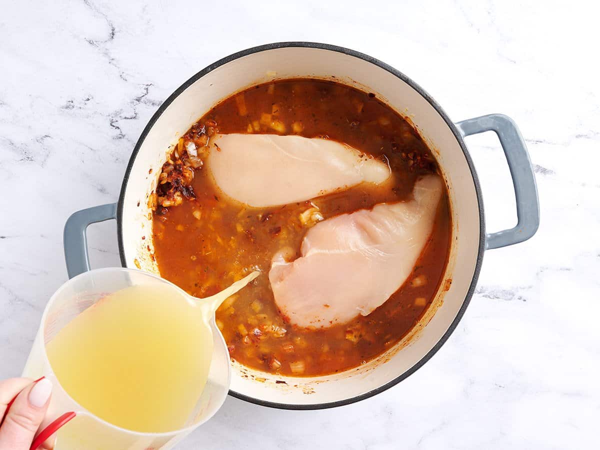 Adding the chicken and the broth to the pot.