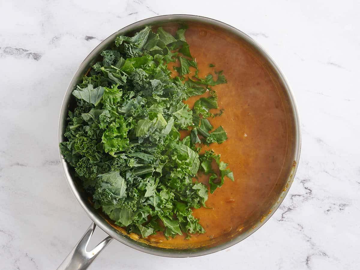 Kale added to a skillet of coconut chickpea curry